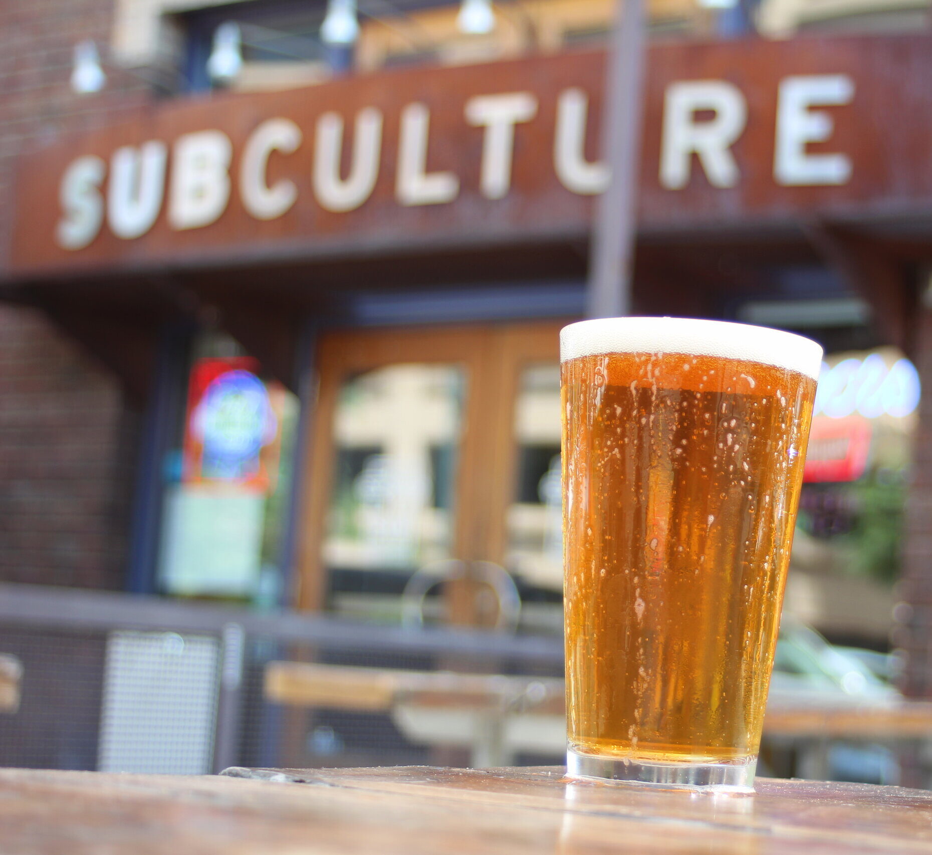 A Cold frothy beer on table with SubCulture sign behind